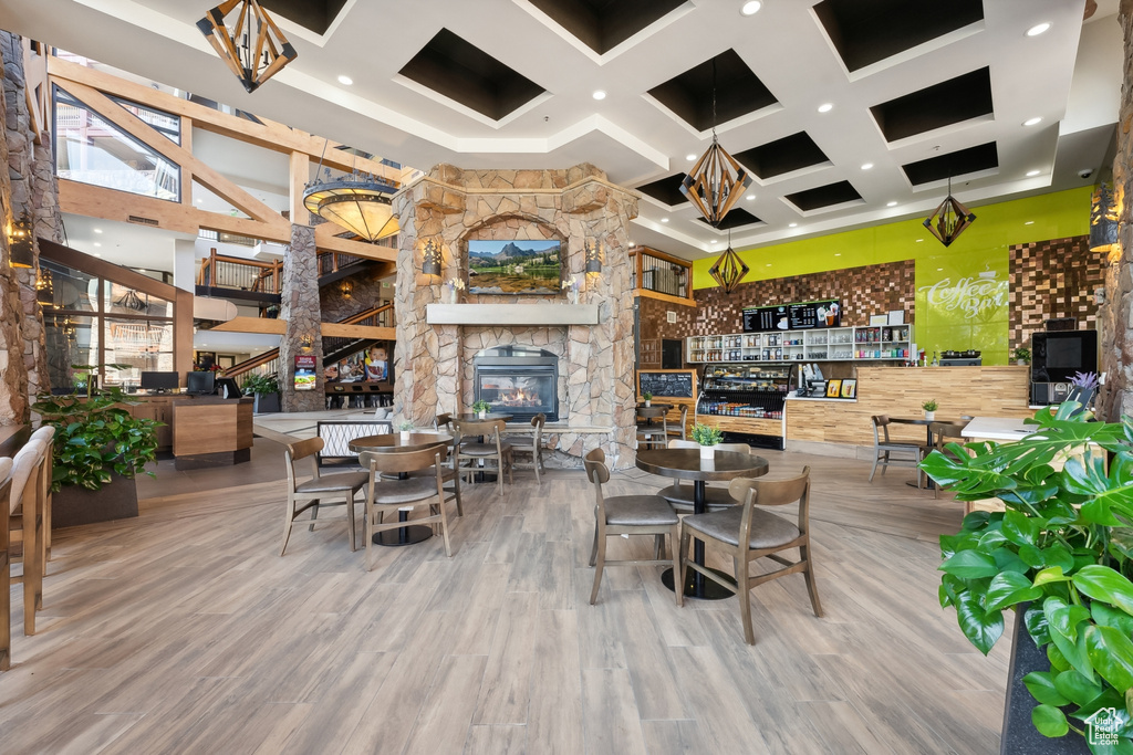 Dining space with a stone fireplace, beamed ceiling, a towering ceiling, and hardwood / wood-style floors