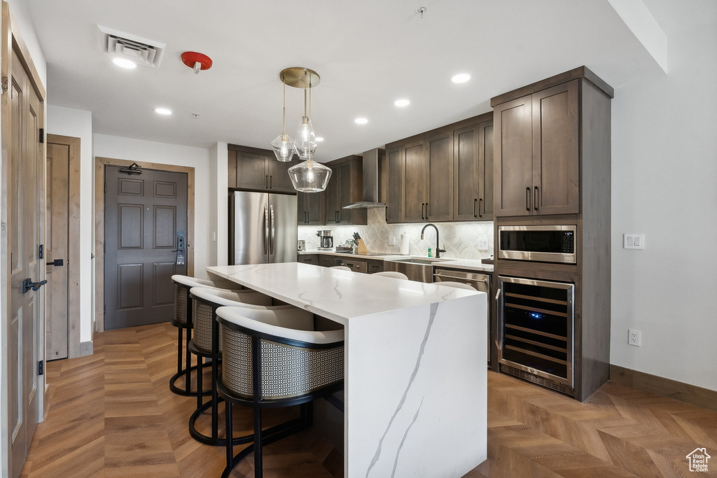 Kitchen with hanging light fixtures, beverage cooler, wall chimney exhaust hood, stainless steel appliances, and a center island