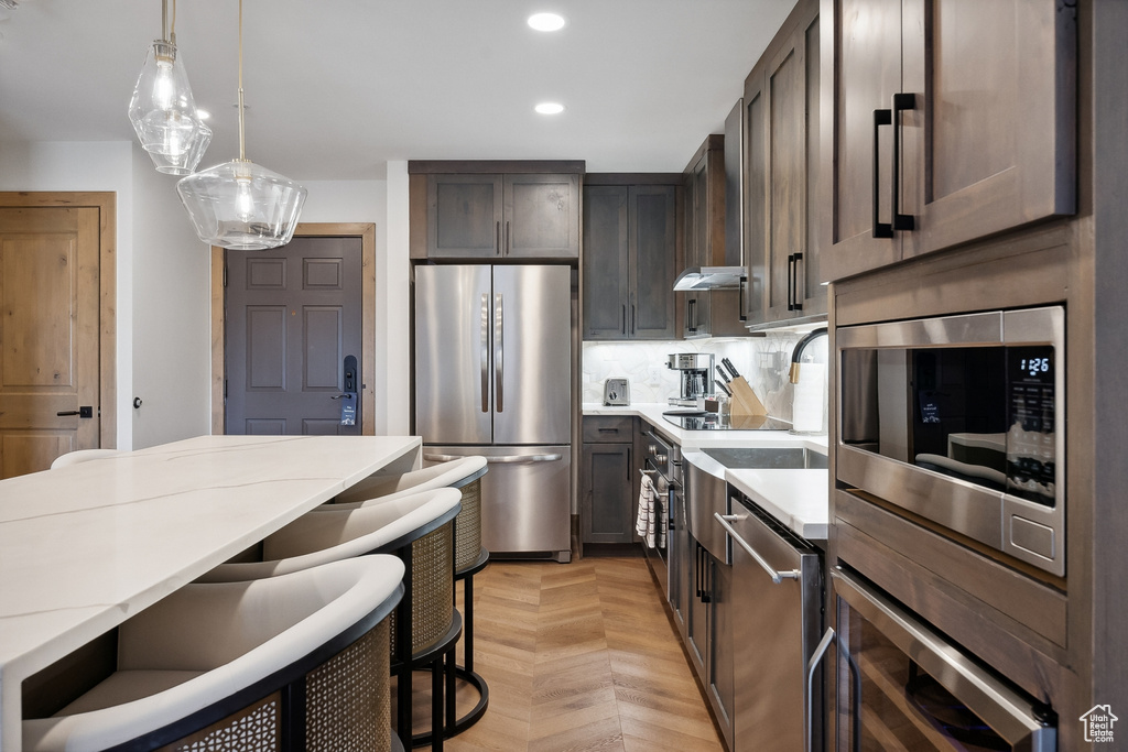 Kitchen with light stone counters, light parquet flooring, dark brown cabinets, decorative light fixtures, and stainless steel appliances