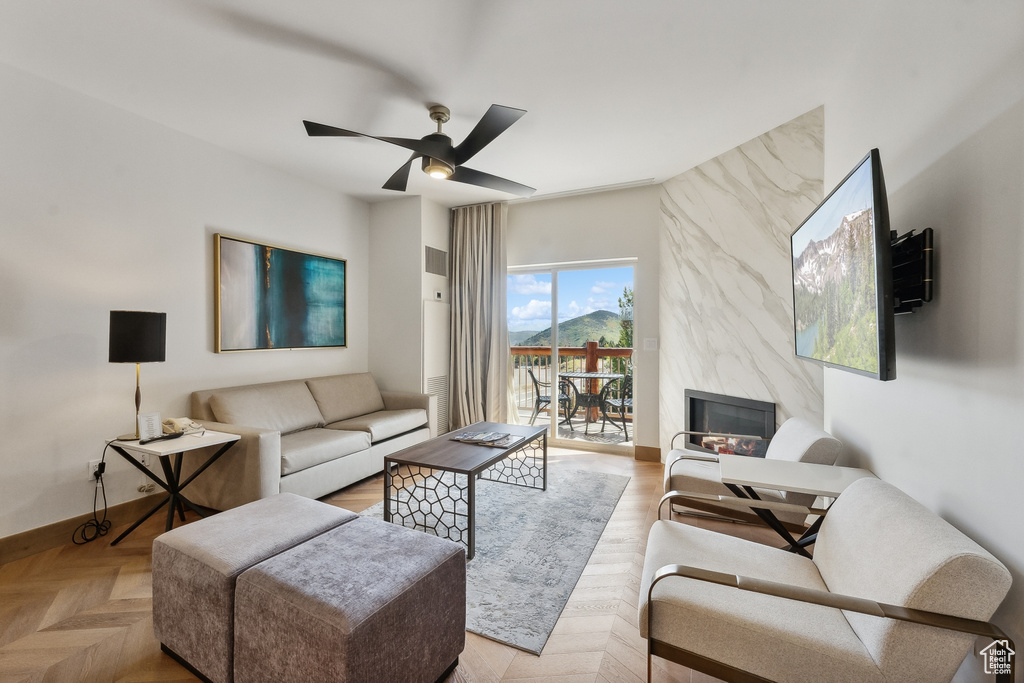 Living room featuring ceiling fan, a fireplace, and light parquet flooring