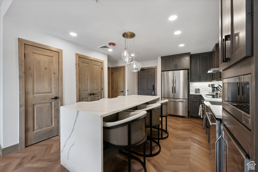 Kitchen featuring light stone counters, parquet floors, a kitchen island, decorative light fixtures, and stainless steel fridge