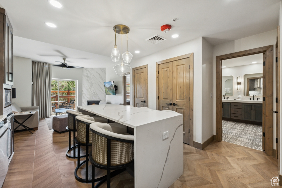 Kitchen with a breakfast bar area, light parquet flooring, decorative light fixtures, light stone countertops, and ceiling fan