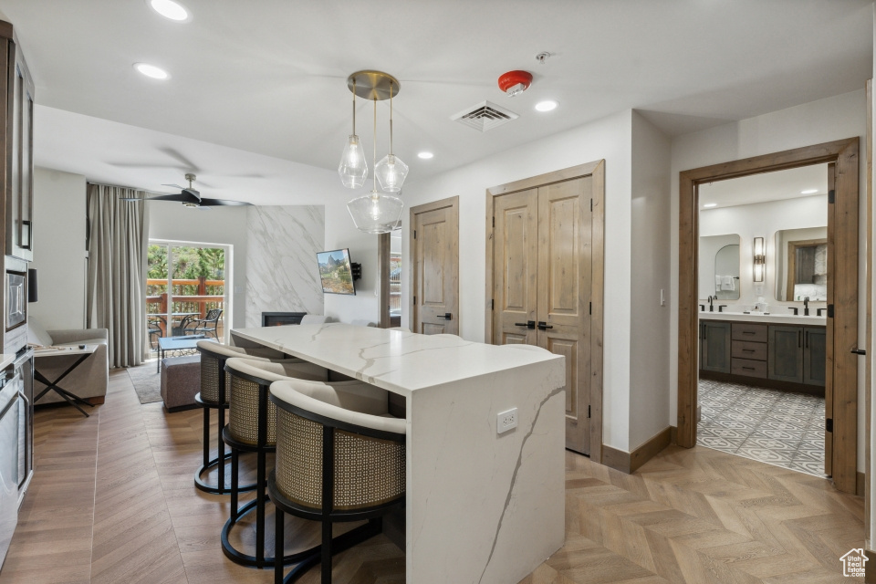 Kitchen with pendant lighting, light stone counters, a kitchen breakfast bar, ceiling fan, and light parquet floors