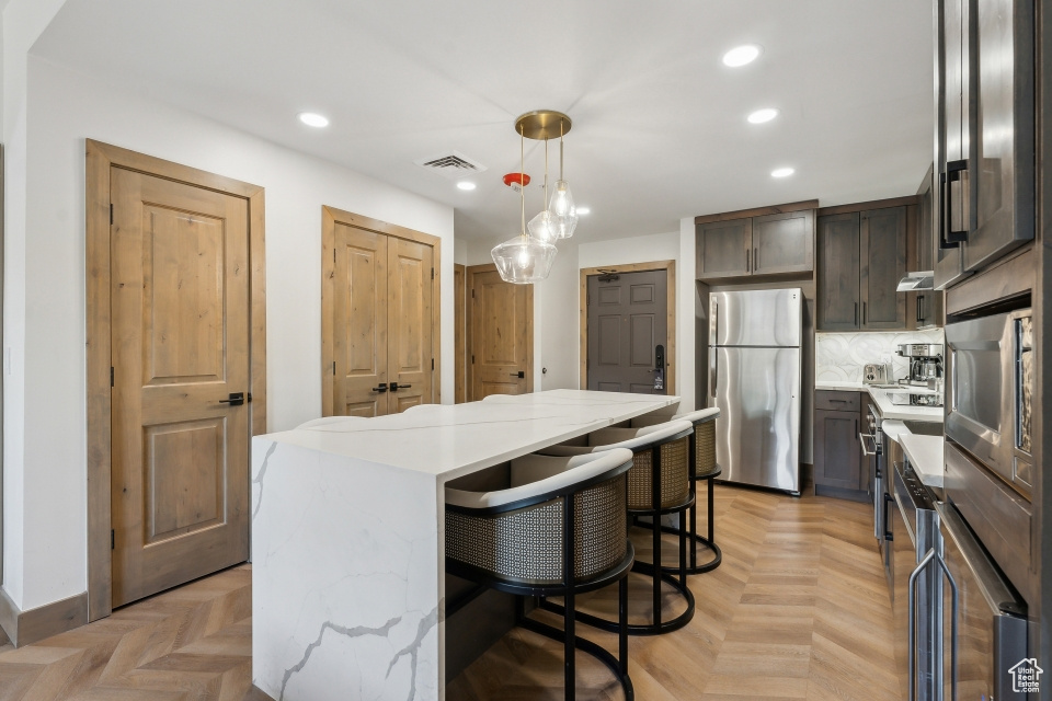 Kitchen featuring hanging light fixtures, light parquet flooring, backsplash, stainless steel appliances, and a center island