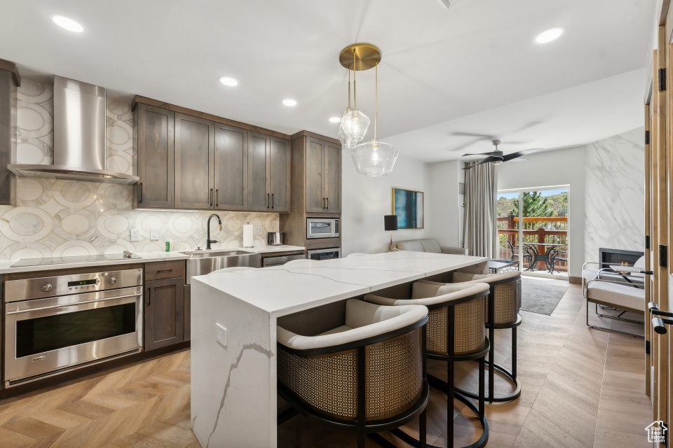 Kitchen featuring light stone counters, wall chimney exhaust hood, stainless steel oven, a center island, and decorative light fixtures