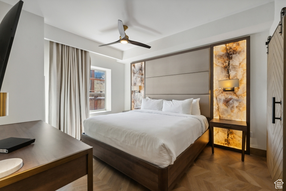 Bedroom with parquet flooring, ceiling fan, and a barn door