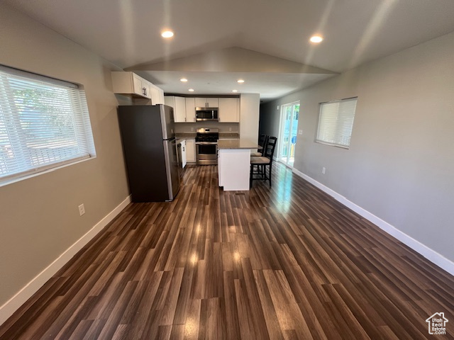 Kitchen featuring appliances with stainless steel finishes, white cabinetry, vaulted ceiling, a center island, and dark hardwood / wood-style floors