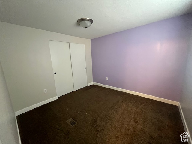 Unfurnished bedroom featuring a closet and dark colored carpet