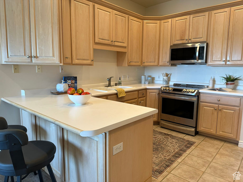 Kitchen with a kitchen breakfast bar, kitchen peninsula, light tile patterned floors, and stainless steel appliances