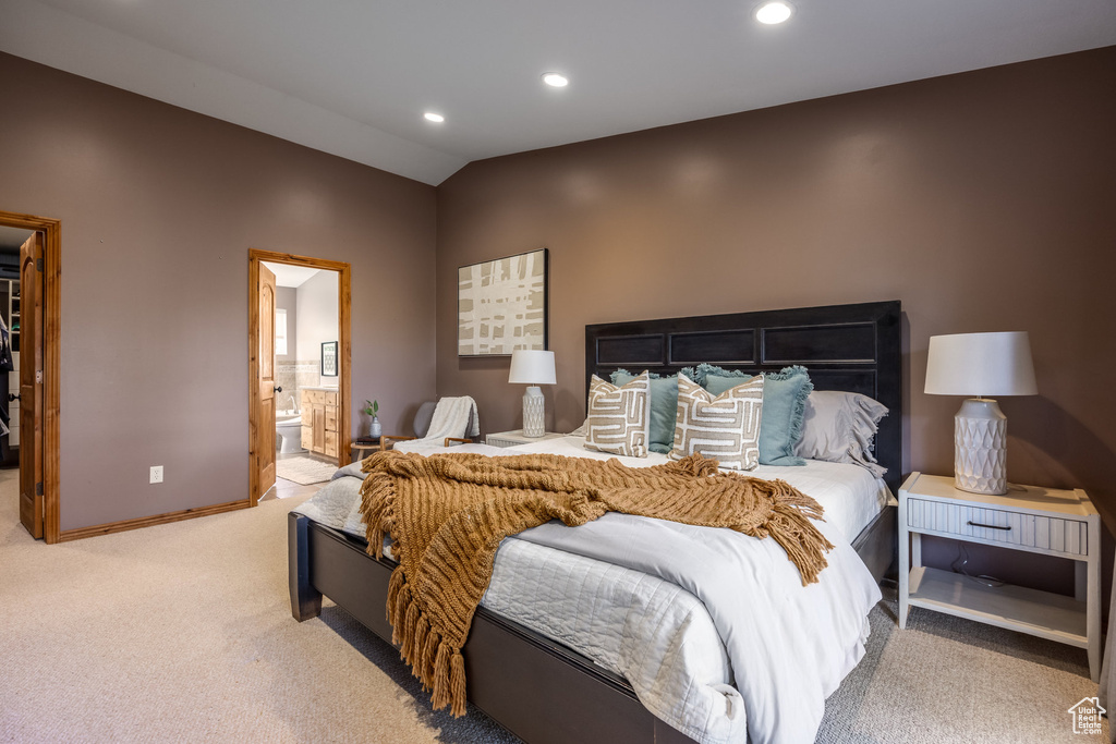 Carpeted bedroom featuring ensuite bathroom and vaulted ceiling