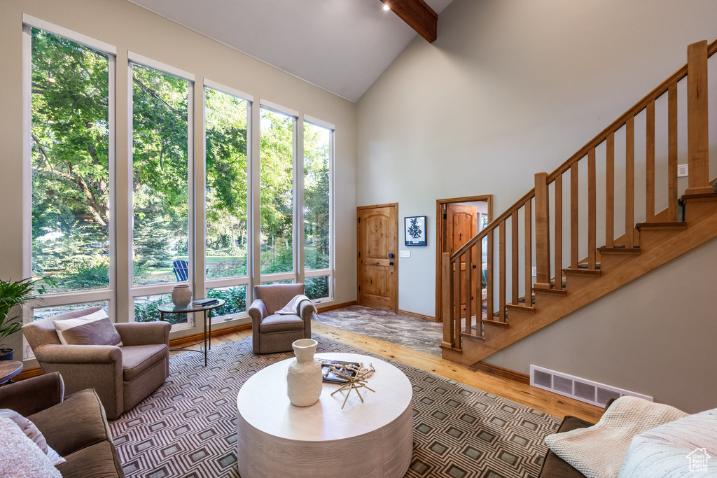 Living room with high vaulted ceiling, a healthy amount of sunlight, beamed ceiling, and light hardwood / wood-style flooring