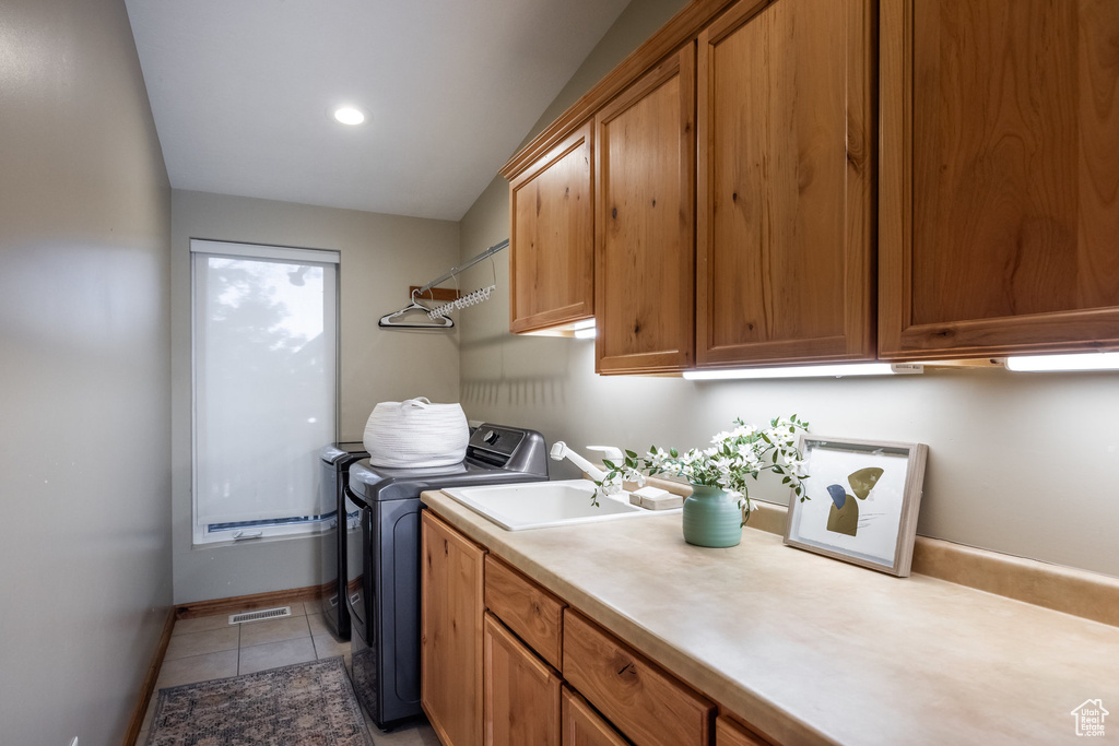 Clothes washing area with washer and dryer, cabinets, sink, and light tile patterned floors