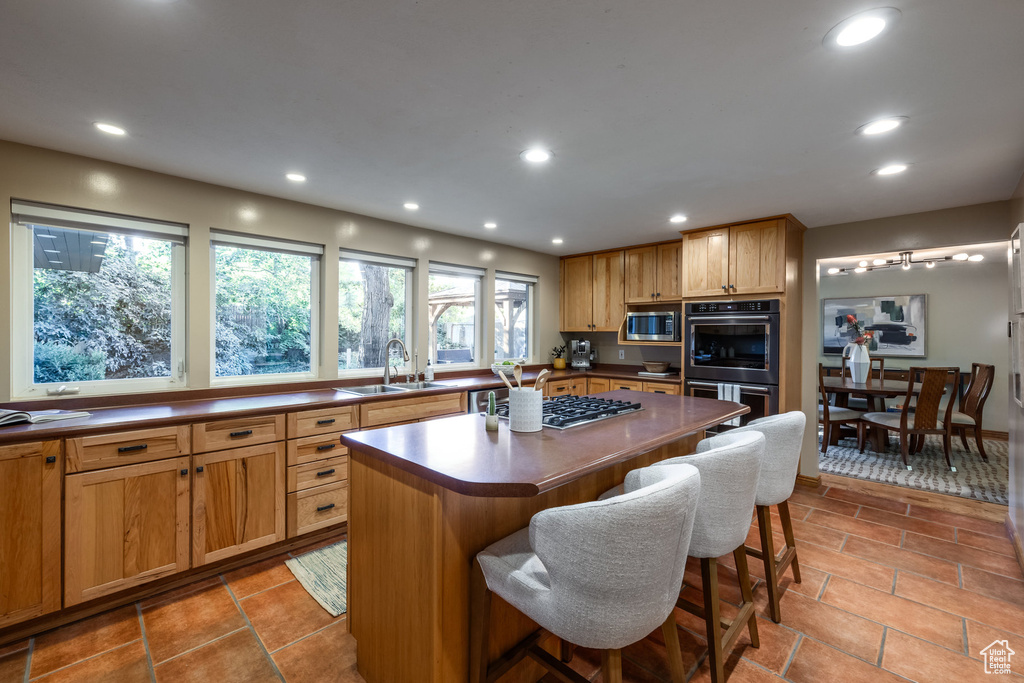 Kitchen featuring light tile patterned floors, a breakfast bar, stainless steel appliances, sink, and a center island