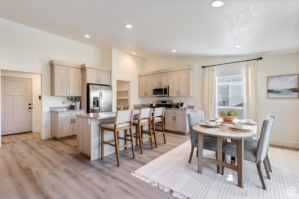 Kitchen with appliances with stainless steel finishes, a kitchen breakfast bar, light hardwood / wood-style floors, lofted ceiling, and a center island