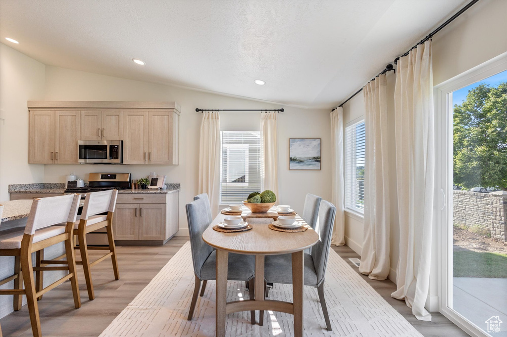Dining space featuring vaulted ceiling, light hardwood / wood-style floors, and a textured ceiling