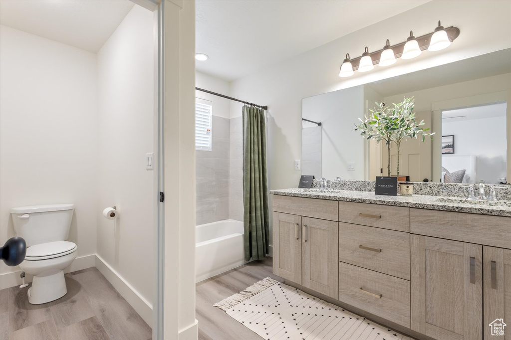 Full bathroom featuring shower / bath combo with shower curtain, vanity, hardwood / wood-style floors, and toilet