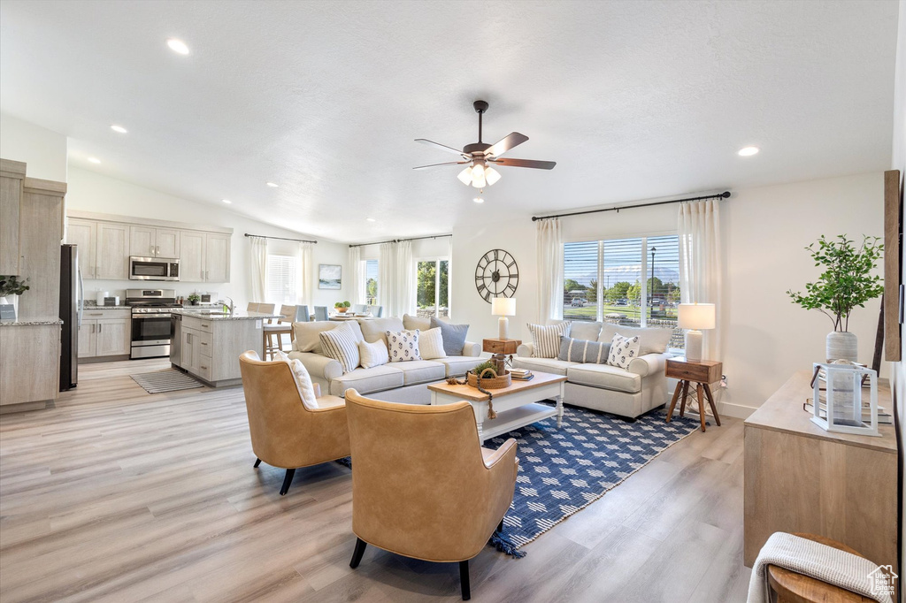Living room with light hardwood / wood-style flooring, lofted ceiling, and ceiling fan
