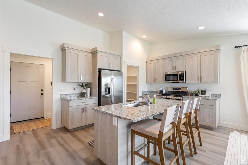 Kitchen with sink, a center island with sink, appliances with stainless steel finishes, light stone countertops, and vaulted ceiling