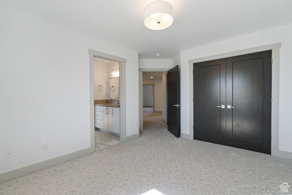 Unfurnished bedroom featuring ensuite bath, sink, light colored carpet, and a closet