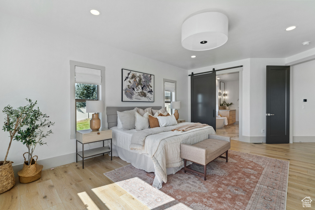 Bedroom featuring ensuite bathroom, light hardwood / wood-style flooring, and a barn door