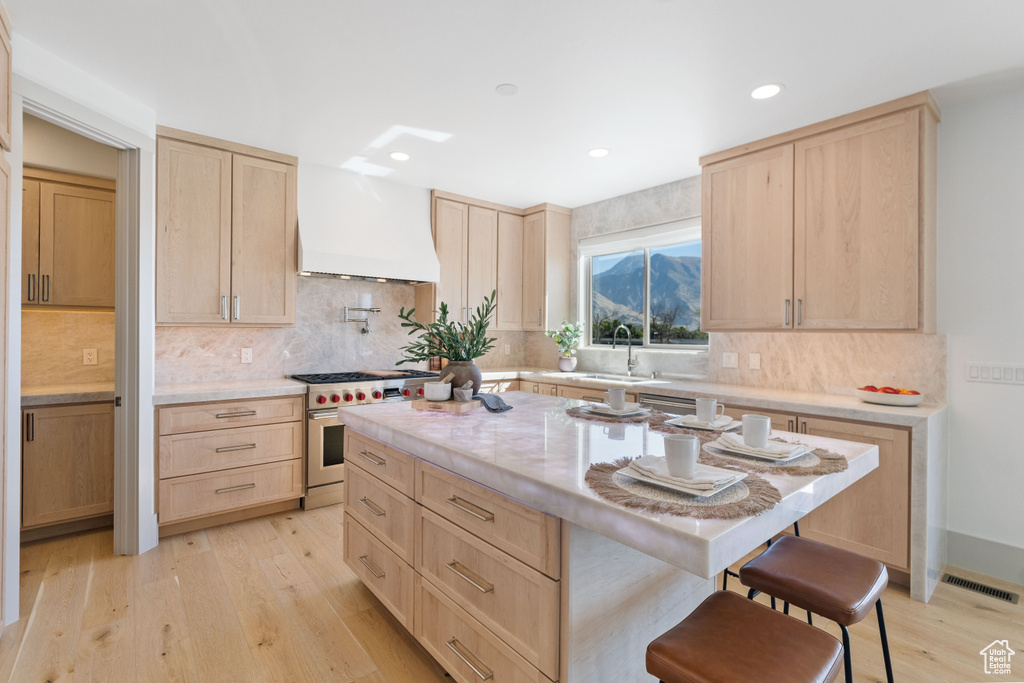 Kitchen featuring a breakfast bar, light hardwood / wood-style floors, custom range hood, luxury range, and light brown cabinetry