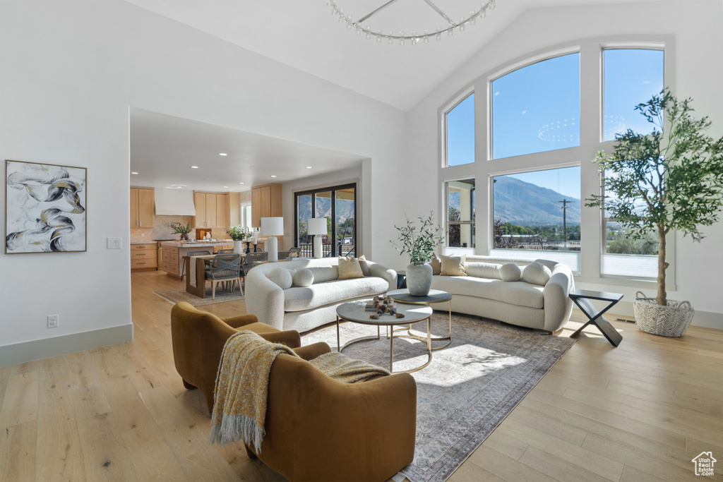 Living room with a notable chandelier, light hardwood / wood-style floors, a mountain view, and high vaulted ceiling