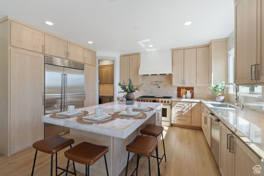 Kitchen with custom range hood, premium appliances, light wood-type flooring, a center island, and sink