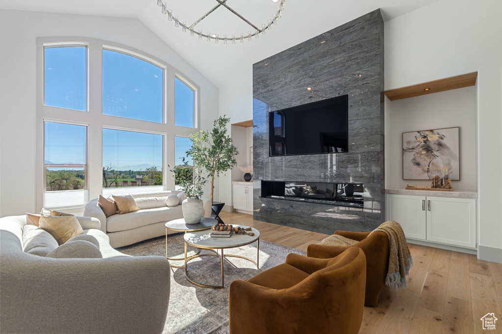 Living room featuring light hardwood / wood-style floors, a fireplace, high vaulted ceiling, and a notable chandelier