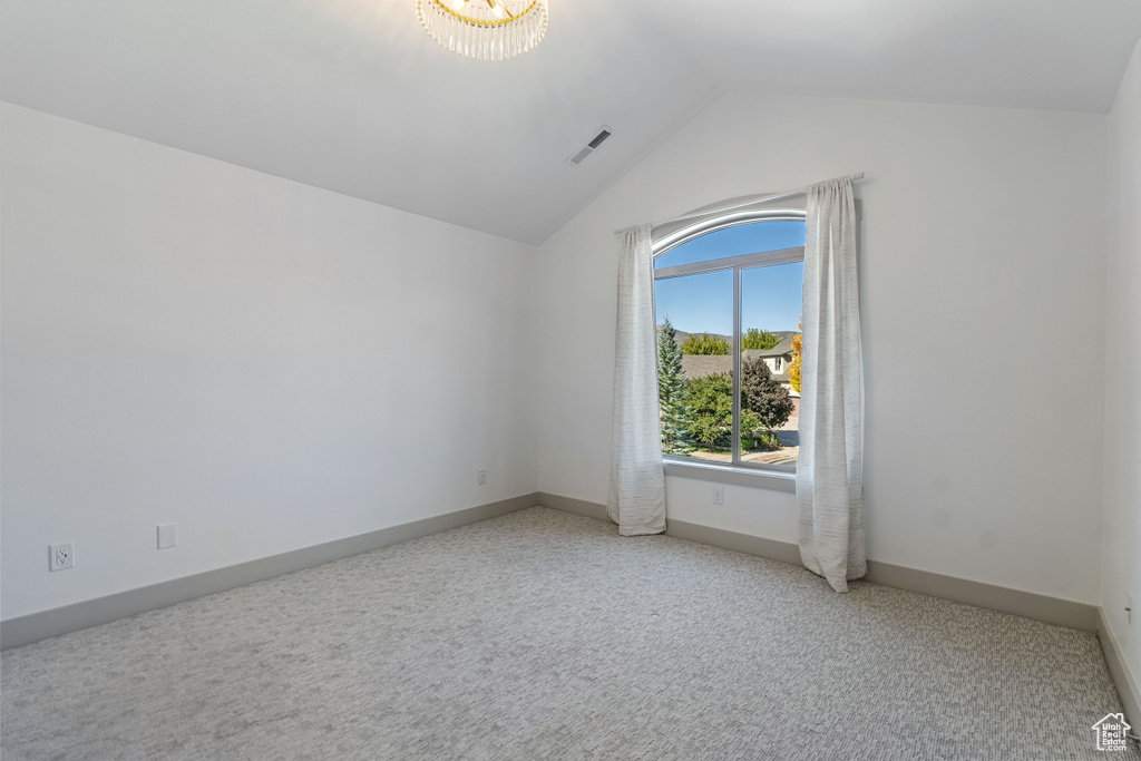 Carpeted spare room with lofted ceiling and a chandelier