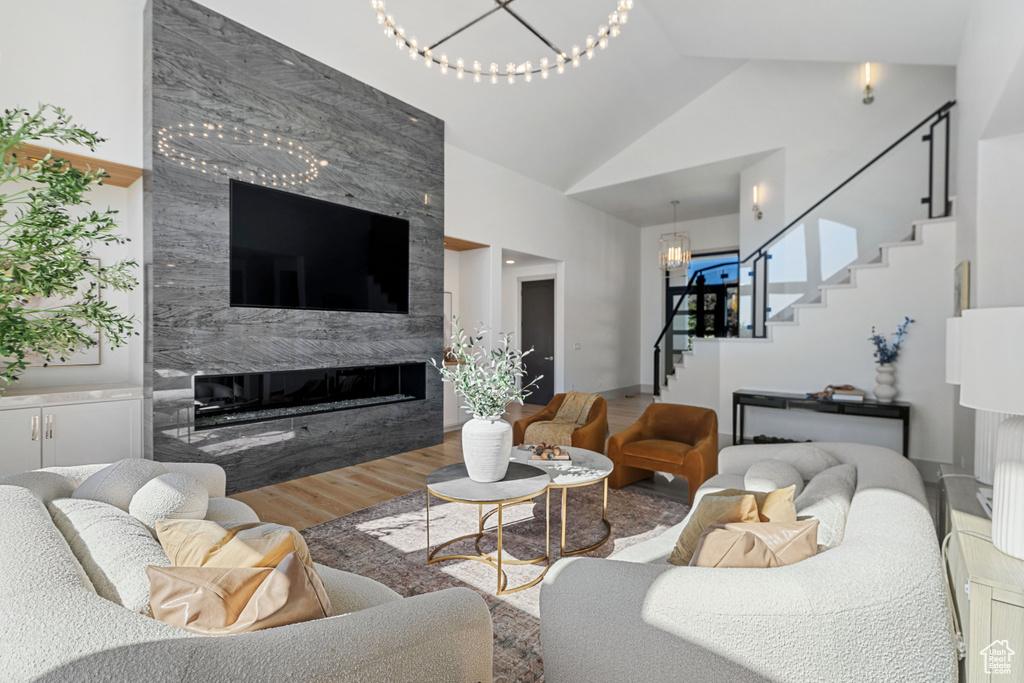 Living room featuring an inviting chandelier, hardwood / wood-style flooring, a premium fireplace, and high vaulted ceiling