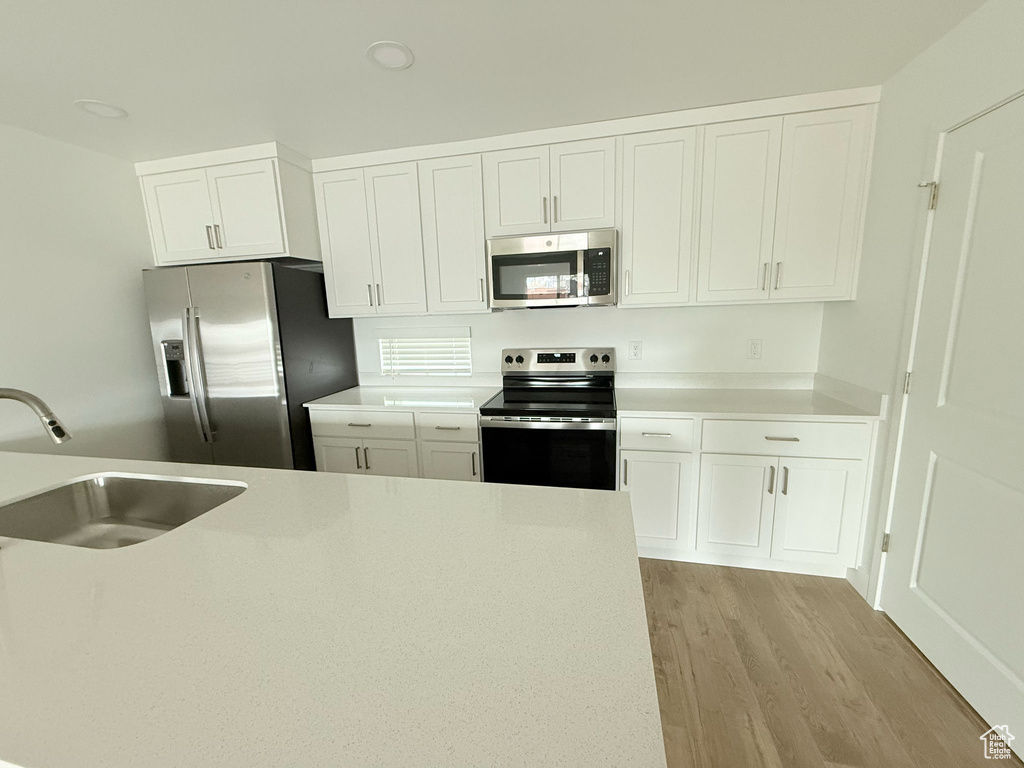 Kitchen featuring a sink, appliances with stainless steel finishes, white cabinets, and light wood finished floors