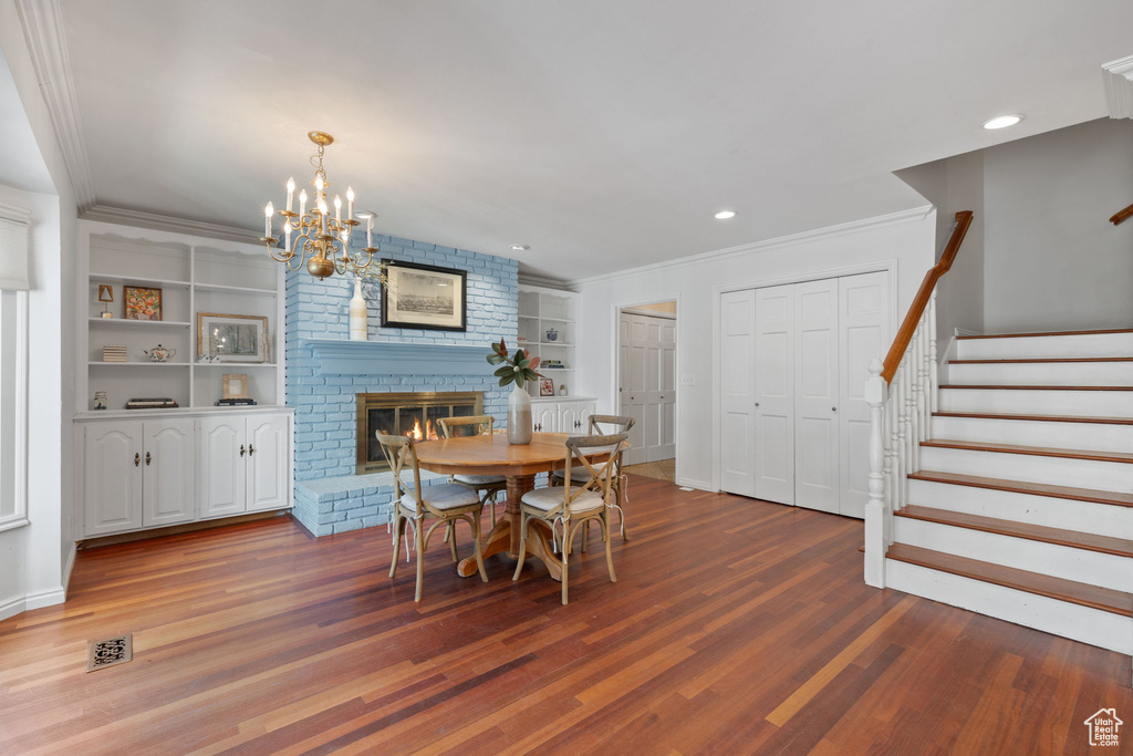 Dining room featuring built in features, a brick fireplace, a chandelier, hardwood / wood-style flooring, and crown molding