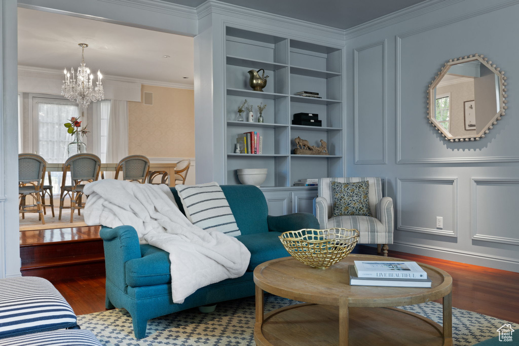 Living room with crown molding, built in shelves, hardwood / wood-style floors, and a notable chandelier