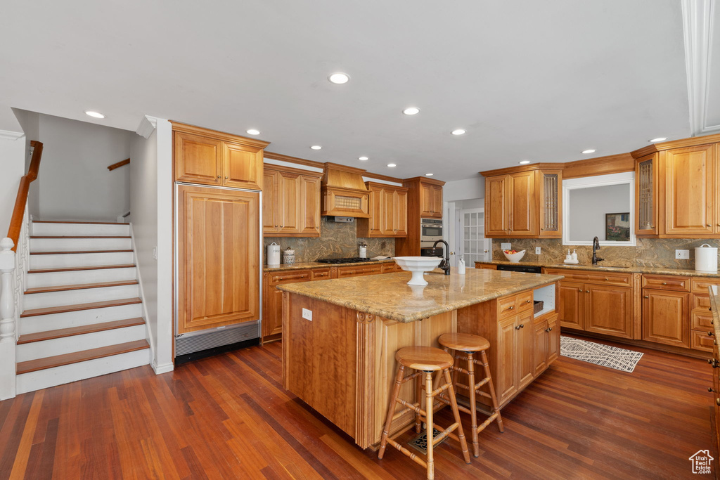 Kitchen with backsplash, a kitchen island with sink, dark wood-type flooring, and a breakfast bar