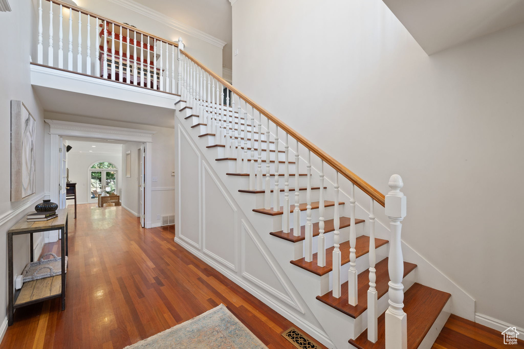 Stairway featuring wood-type flooring, ornamental molding, and a high ceiling