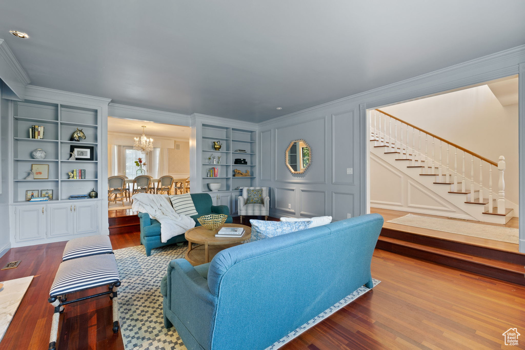 Living room with an inviting chandelier, wood-type flooring, built in features, and crown molding