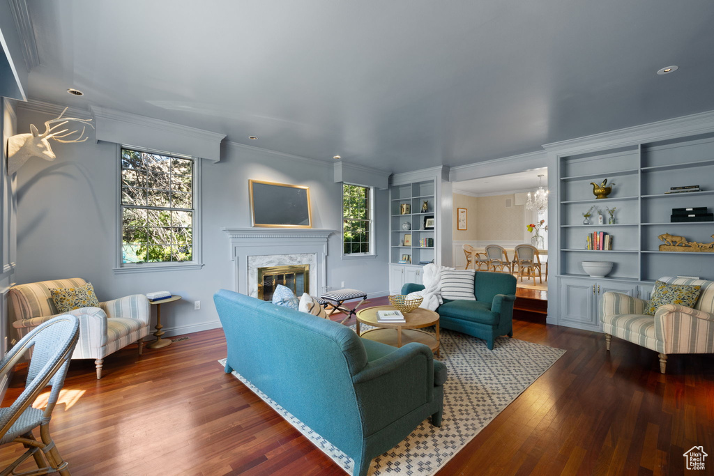 Living room featuring built in features, ornamental molding, a chandelier, dark wood-type flooring, and a fireplace