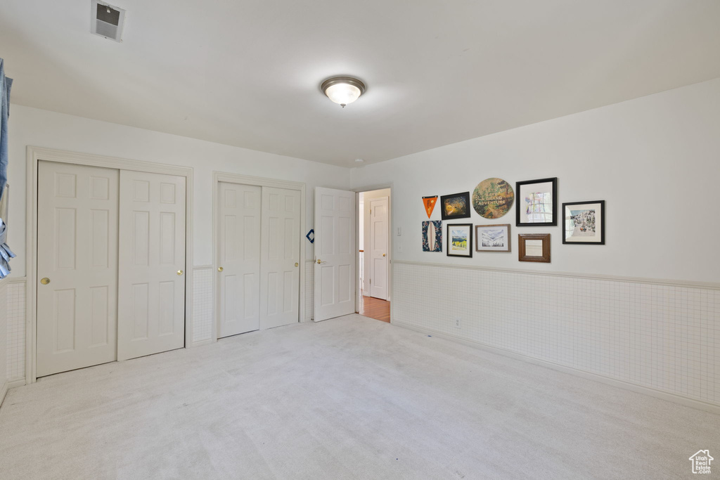 Unfurnished bedroom featuring light carpet and two closets