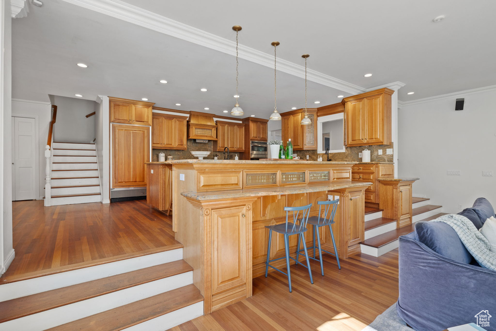 Kitchen featuring a breakfast bar, ornamental molding, light hardwood / wood-style flooring, and tasteful backsplash