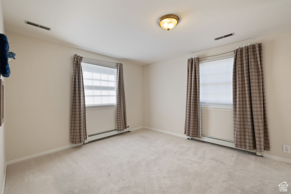 Empty room with a baseboard heating unit and light colored carpet