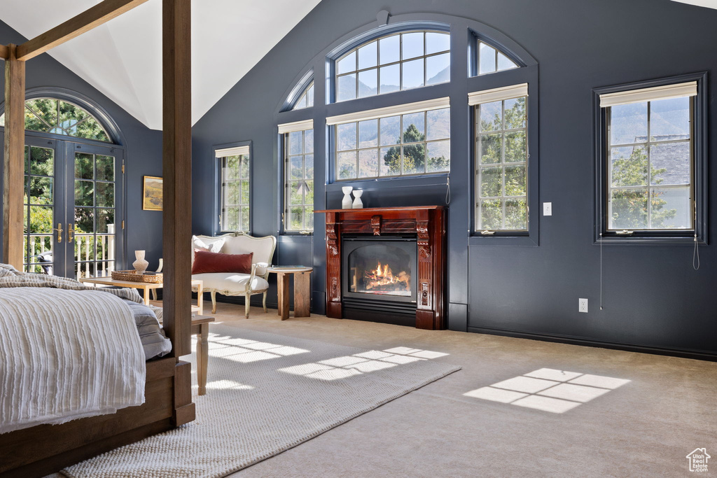 Carpeted bedroom with high vaulted ceiling, multiple windows, and french doors