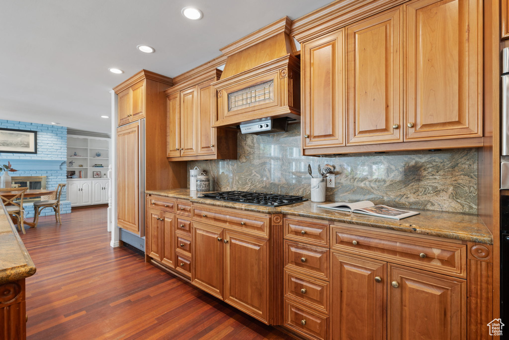 Kitchen featuring dark hardwood / wood-style floors, tasteful backsplash, stainless steel gas cooktop, a fireplace, and custom range hood