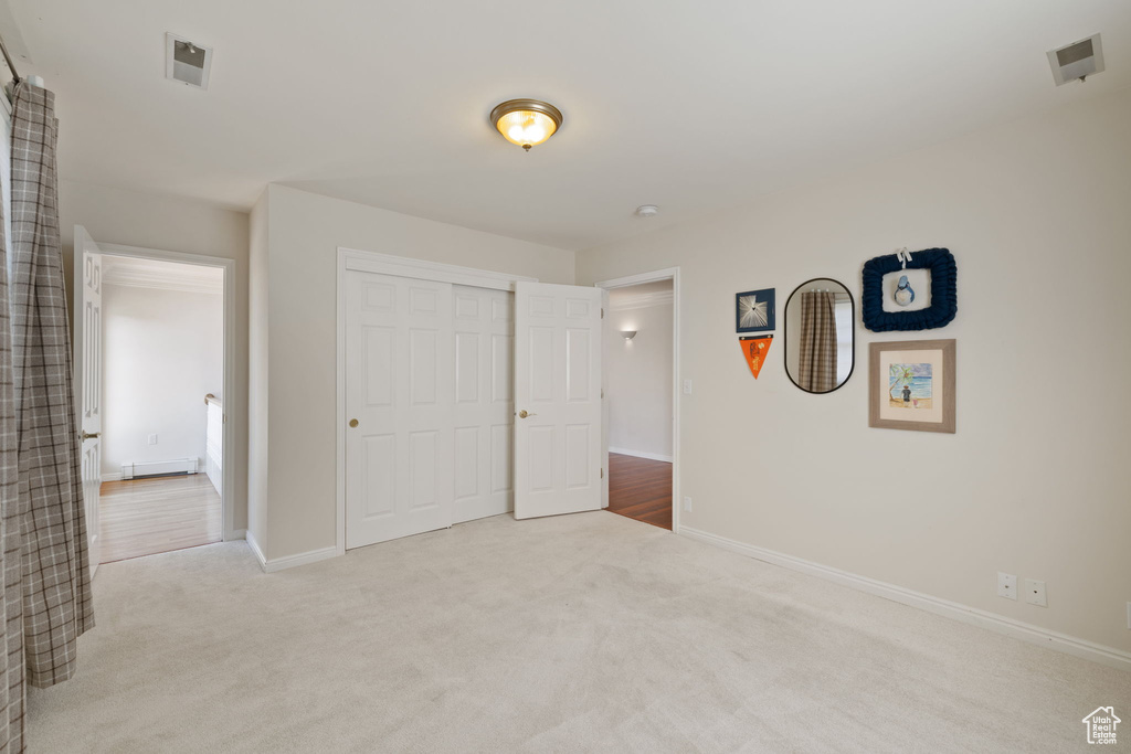 Unfurnished bedroom with light carpet, a closet, and baseboard heating