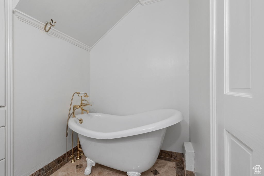 Bathroom with ornamental molding, lofted ceiling, a tub, and tile patterned floors