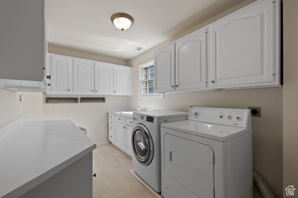 Clothes washing area featuring cabinets, light carpet, washer and dryer, and sink