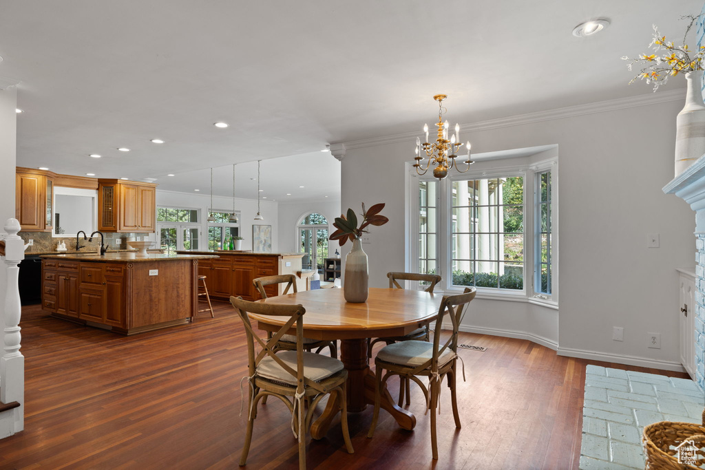 Dining area with dark hardwood / wood-style floors, sink, a notable chandelier, a fireplace, and crown molding