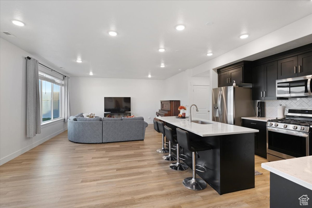 Kitchen featuring appliances with stainless steel finishes, a kitchen breakfast bar, light hardwood / wood-style flooring, a kitchen island with sink, and sink