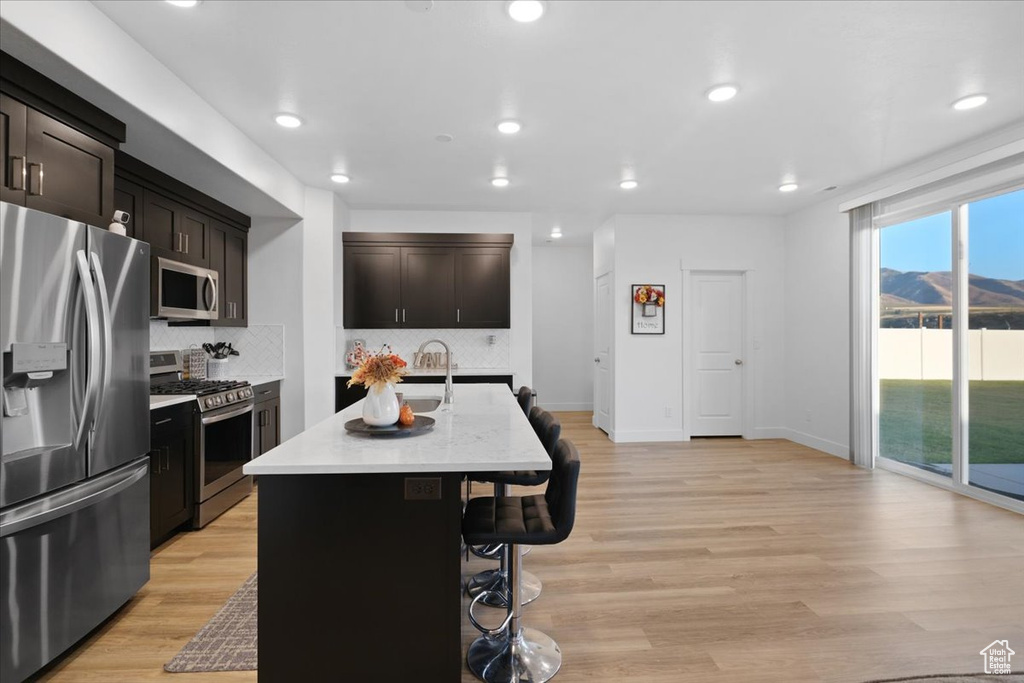 Kitchen with an island with sink, tasteful backsplash, appliances with stainless steel finishes, a breakfast bar, and light wood-type flooring