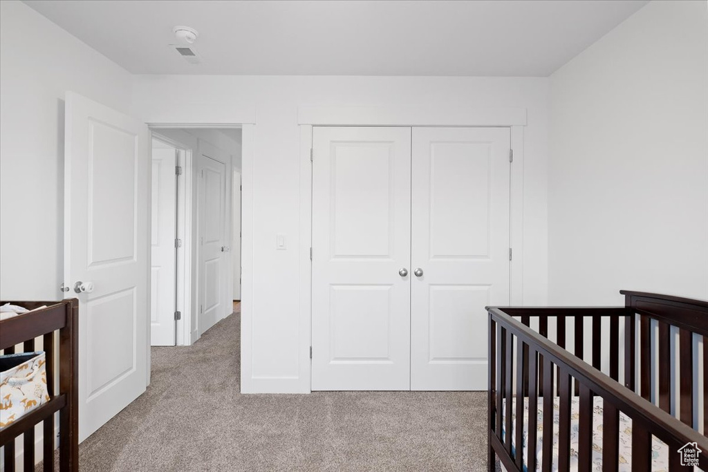 Bedroom featuring light carpet, a closet, and a nursery area