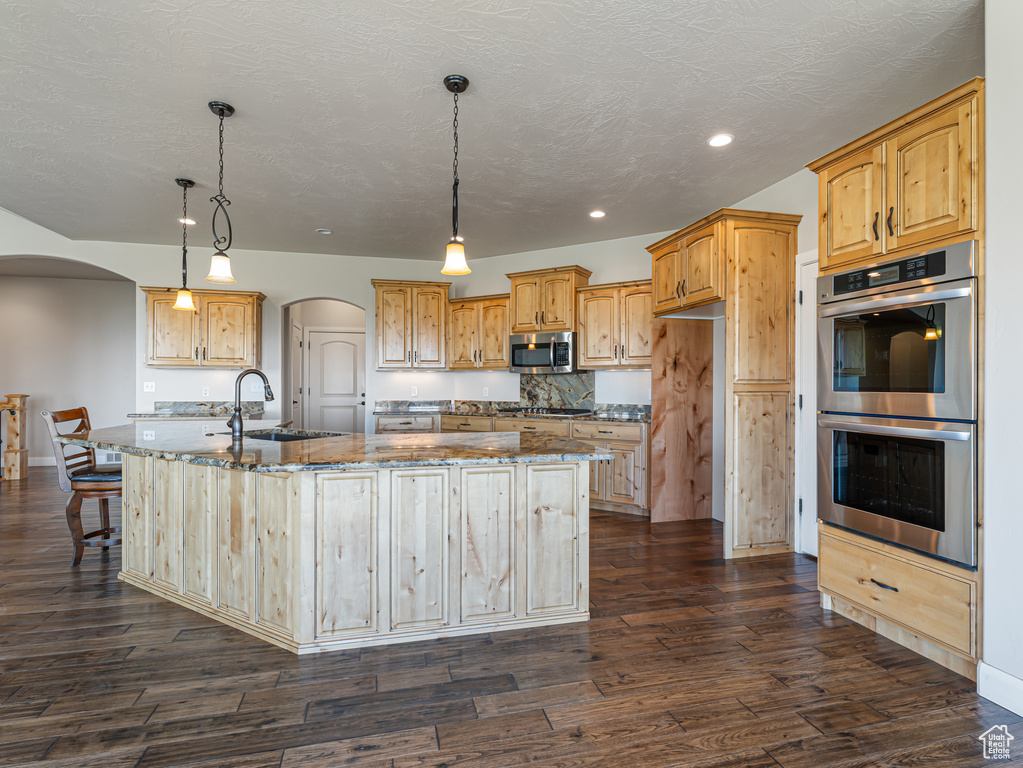 Kitchen featuring stone countertops, arched walkways, a large island, and appliances with stainless steel finishes